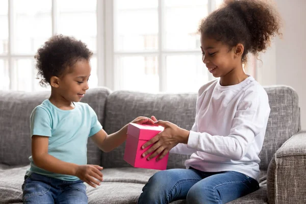 Cuidar da menina afro-americana caixa de presente para o irmão pequeno — Fotografia de Stock