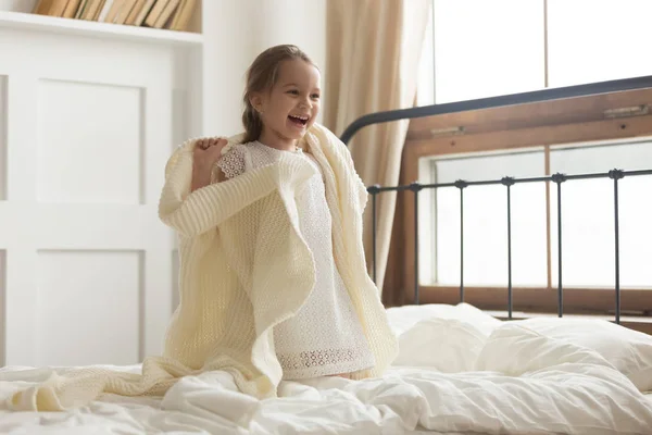 Gadis anak bahagia ditutupi dengan rajutan kotak-kotak tertawa di tempat tidur — Stok Foto