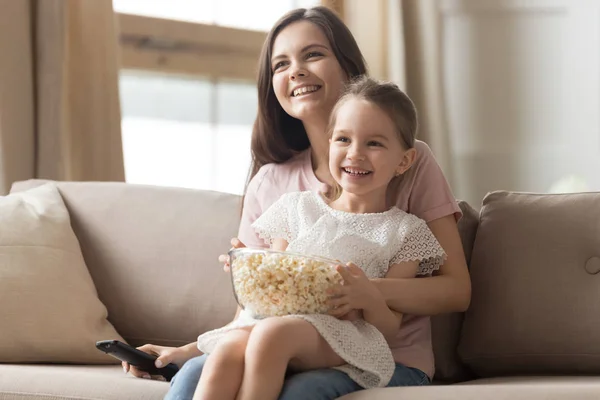 Feliz mamá y niña riendo viendo la televisión en el sofá —  Fotos de Stock