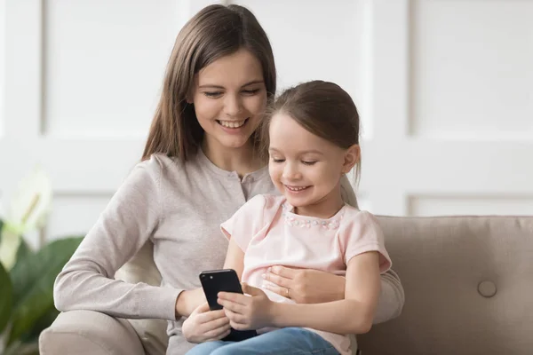 Criança feliz filha e mãe gostam de usar o telefone no sofá — Fotografia de Stock