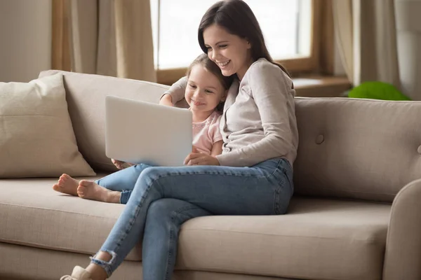 Sorrindo mãe assistindo desenhos animados on-line no laptop com filha criança — Fotografia de Stock