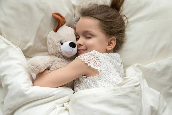 Gadis kecil yang lucu memeluk boneka beruang tidur di tempat tidur — Stok Foto