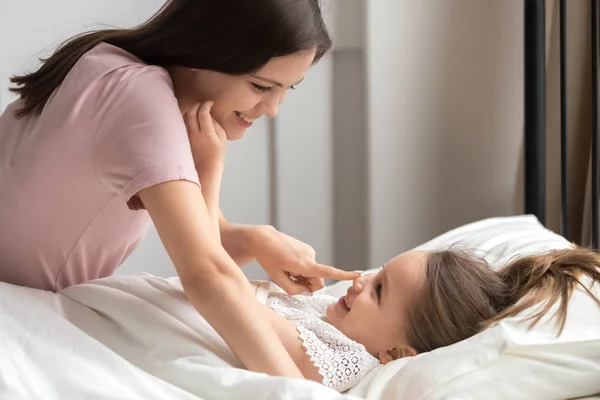 Ibu yang bahagia dengan lembut membangunkan anak perempuan lucu di tempat tidur — Stok Foto