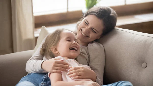 Щаслива мама обіймає дитину дочка сміється разом лежачи на дивані — стокове фото