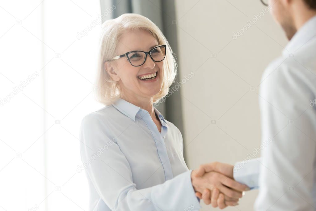 Happy mature businesswoman handshaking partner client, trust and gratitude handshake