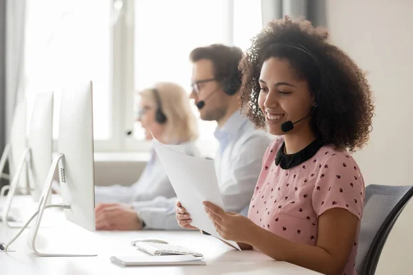 Smiling african woman call center operator wearing headset reading papers — Stock Photo, Image