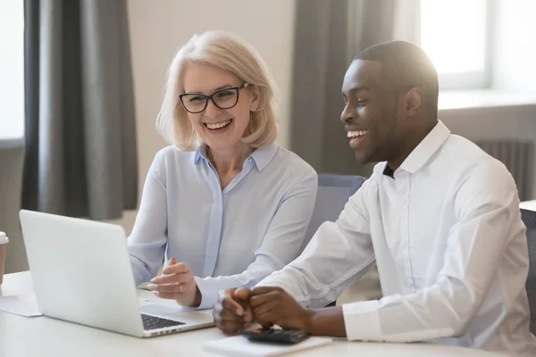 Happy african and caucasian colleagues talking in office at laptop — Stock Photo, Image