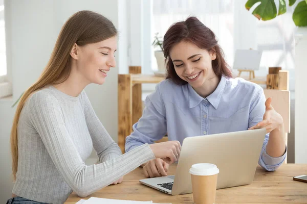 Tusenåriga kvinnor tittar på dator leende sitter på kontor — Stockfoto