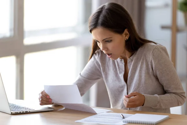 Surprised young woman sitting at desk reading letter — Stock Photo, Image