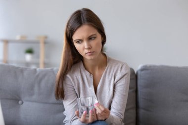 Frustrated pensive woman holding pill and glass of water clipart