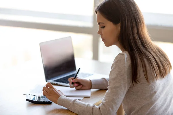 Side rear view young female sitting at table calculating money — Stock Photo, Image