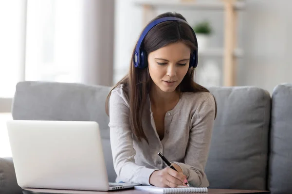 Woman in headphones sitting on couch e-learning writing notes — Stock Photo, Image