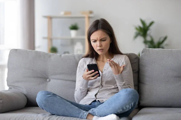 Chica confundida sintiéndose molesto leyendo malas noticias en el teléfono móvil — Foto de Stock