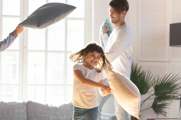Vrolijke familie en dochtertje spelen met kussens thuis — Stockfoto