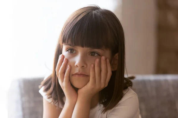 Расстроенная маленькая девочка, сидящая дома на диване, чувствует себя несчастной — стоковое фото