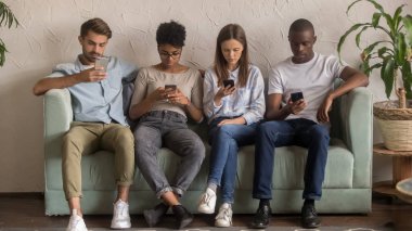 Çok kültürlü insanlar kanepede oturan birbirlerini görmezden akıllı telefonlar kullanarak