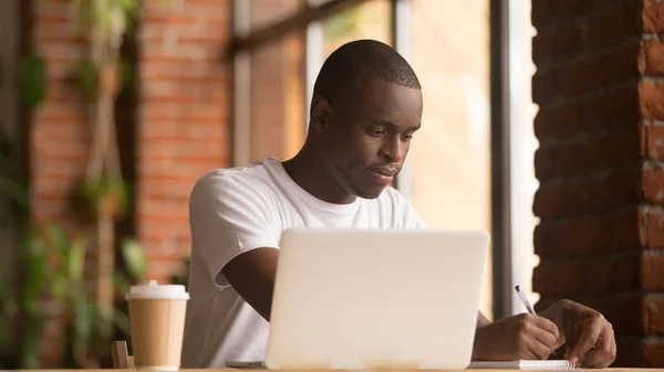 Serious african american man working studying with laptop making notes — Stock Photo, Image