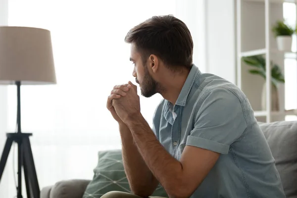 Pensativo hombre serio sentado en el sofá en casa, perdido en pensamientos — Foto de Stock