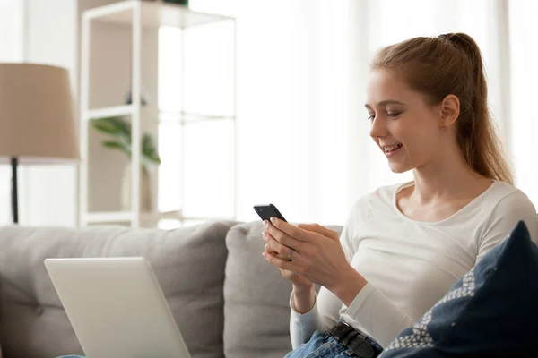 Smiling woman using phone, mobile device app, sitting on sofa — Stock Photo, Image