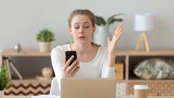 Geïrriteerde jonge vrouw met behulp van telefoon op de werkplek, het lezen van slecht nieuws — Stockfoto