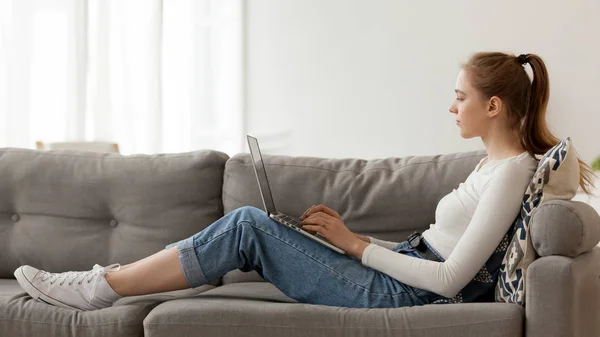 Femme détendue utilisant un ordinateur portable, travaillant, faisant du shopping sur Internet, assise sur un canapé — Photo