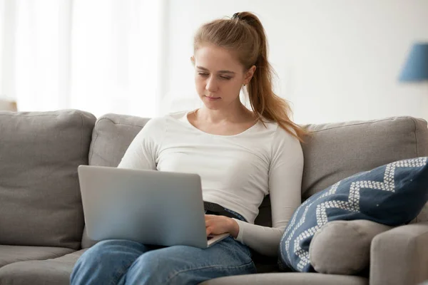 Femme sérieuse travaillant, utilisant un ordinateur portable, tapant, assise seule sur le canapé — Photo