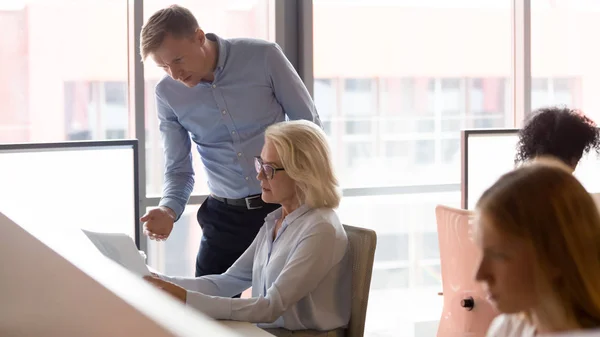 Seriös chefs mentor som hjälper gammal medarbetare med pappers arbete på kontoret — Stockfoto