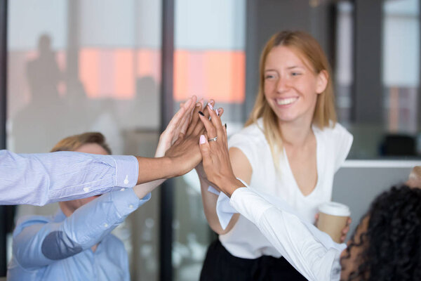 Happy multicultural employees give high five together, focus on hands