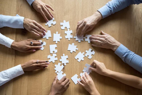 Diverse business team assemble puzzle together connect pieces at desk