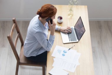 Ofiste telefonda konuşurken dizüstü bilgisayar kullanarak iş kadını, üst görünüm