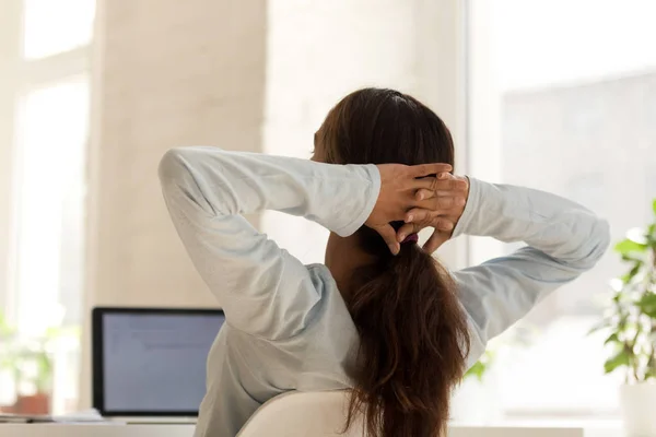 Woman relaxing on chair at work holding hands behind head