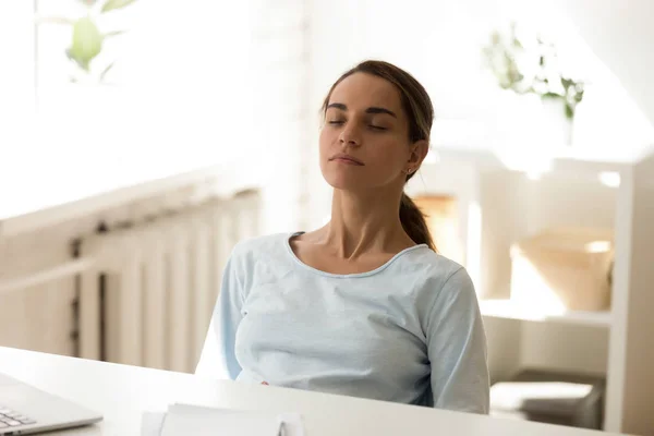 Calm stress free woman sitting at desk with eyes closed