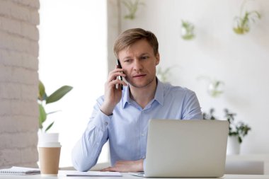 Kapalı alanda oturan ve cep telefonuyla konuşan işadamı.