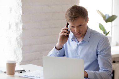 Dizüstü bilgisayarda çalışan ve akıllı telefonda konuşan yönetici