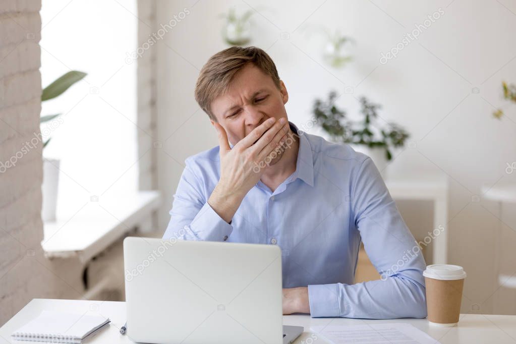 Tired businessman yawning at workplace near laptop