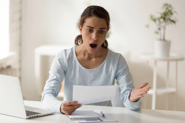 Mujer conmocionada y confundida mirando el papel en el escritorio — Foto de Stock