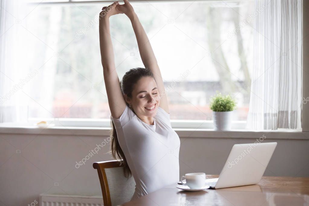 Happy relaxing woman stretching in front of computer at home