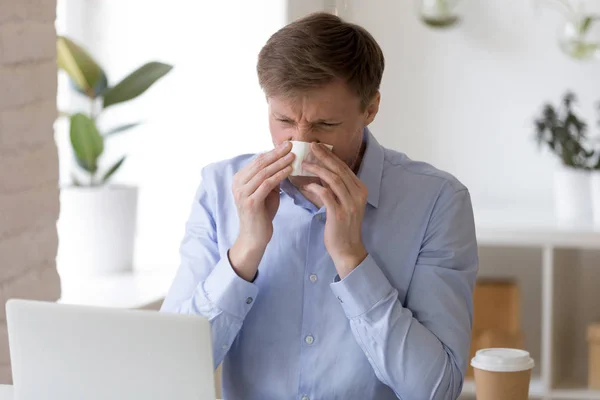 Хворий чоловік сидить в офісі і чхає носом . — стокове фото
