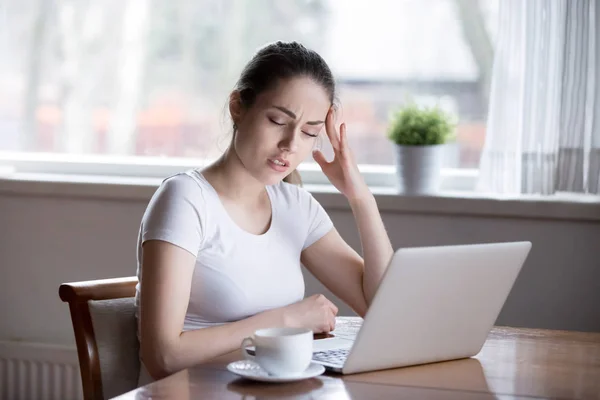 Молода красива жінка має головний біль, що працює на комп'ютері вдома — стокове фото