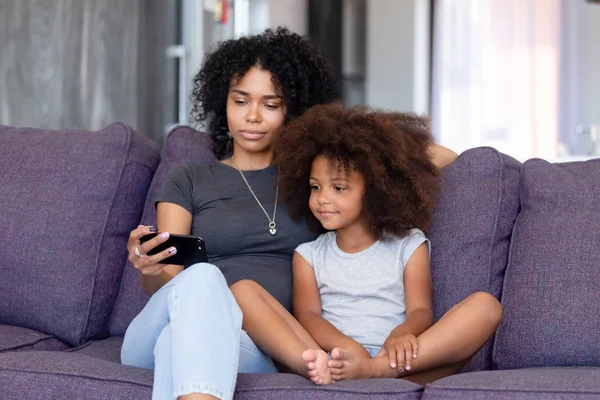 African American kobieta z córką za pomocą telefonu razem w domu — Zdjęcie stockowe