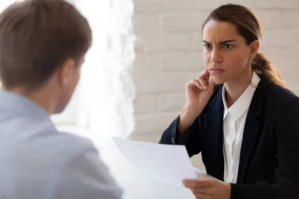 Forretningsdame ser mistenkelig ut mens hun leser CV-en på jobbintervju – stockfoto