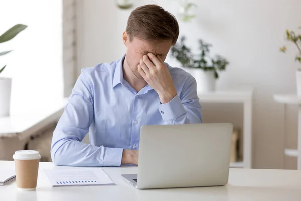 Millenial man massaging his nose at workplace — Stock Photo, Image