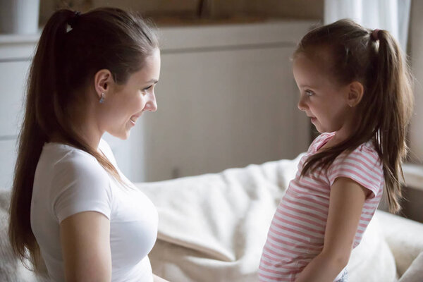 Счастливая мать смотрит на улыбающуюся дочь, держащую ее за руки
