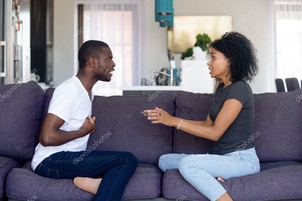 Unhappy African American couple quarreling, sitting on sofa at home