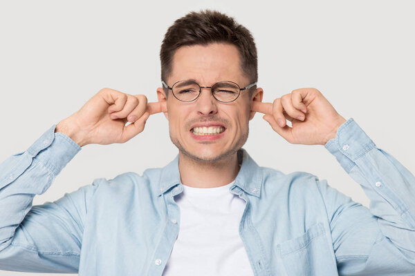Annoyed man in glasses cover ears avoiding loud sound