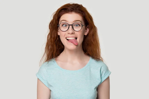 Funny red-haired girl in glasses play childish showing tongue — Stock Photo, Image