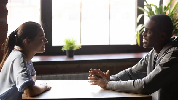 Diversos millennial positivo pareja sentado a la mesa de chat se siente bien —  Fotos de Stock