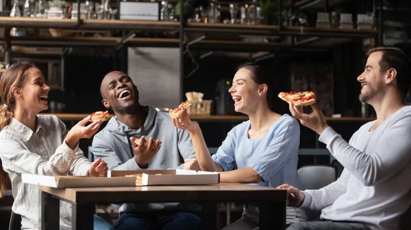 Amici multirazziali che ridono mangiando pizza riuniti in pizzeria — Foto Stock