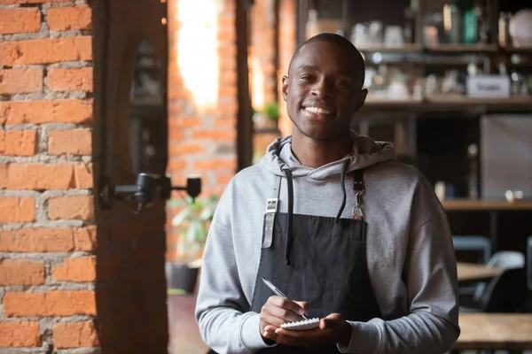 Sonriente camarero africano de pie en el interior mirando a la cámara — Foto de Stock