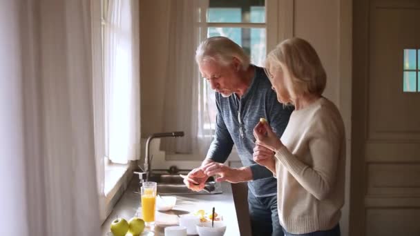 Щаслива любляча старша зріла пара весело готує здоровий сніданок — стокове відео